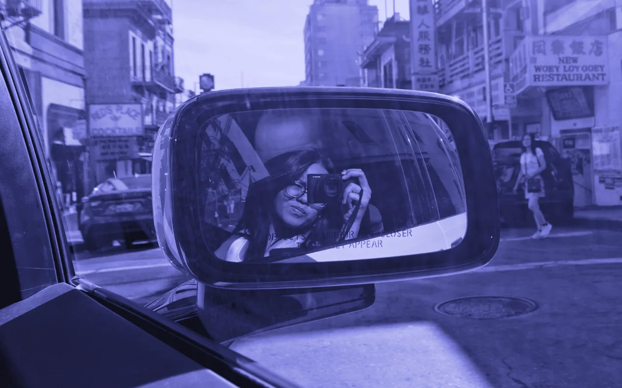 Felicia photographing the street with a compact camera, reflected in a car wing mirror in San Francisco's Chinatown.